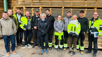 LAB-ammattikorkeakoulun täydennyskoulutukseen osallistuneet Iisveden Metsän työntekijät poseeraavat yhdessä lehtori Markku Levasen kanssa puutuotepinon edessä hymyssä suin.