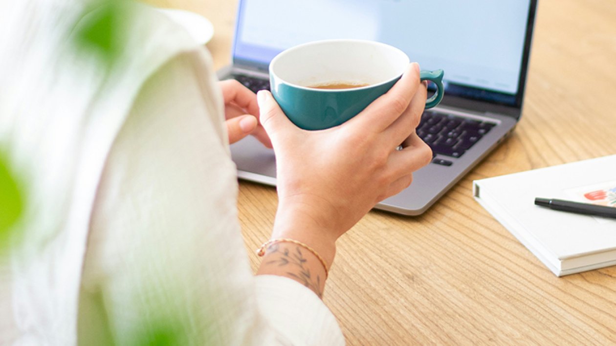 Woman studying on a laptop and a coffee cup on a hand.