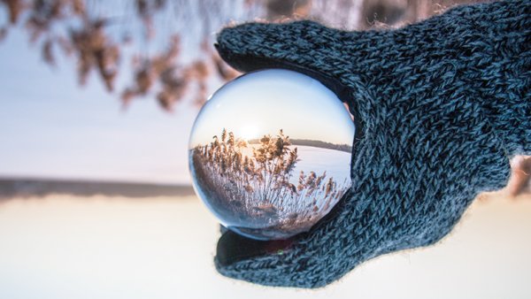 A hand holding a glass ball in a winter landscape